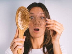 Uma mulher com expressão de surpresa segura um tufo de cabelo que se desprendeu na escova. A imagem representa o choque e a preocupação com a queda de cabelo pós-parto.