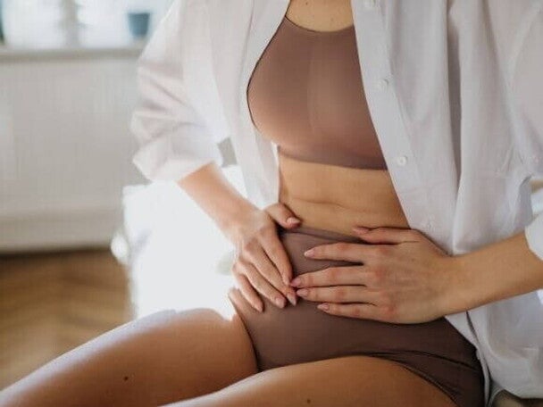 Mulher sentada com as mãos sobre o abdômen, sentindo dor pélvica