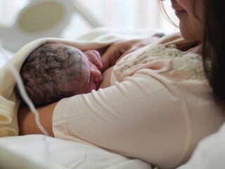 Uma mãe recém-parturiente, usando um roupão hospitalar, amamentando seu bebê recém-nascido. Uma mãe recém-parturiente, usando um roupão hospitalar, amamentando seu bebê recém-nascido.