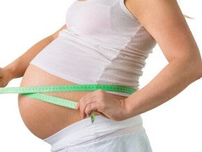 Mulher grávida de 33 semanas de gravidez medindo a circunferência da barriga com fita métrica, um marco no terceiro trimestre.