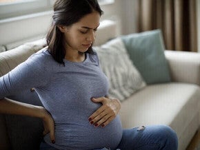 Mulher grávida com náusea, sentada no sofá