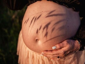 Pessoa grávida acariciando a barriga ao ar livre