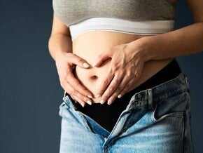 Abdômen de uma mulher grávida no primeiro ou segundo trimestre, mãos em formato de coração sobre a barriga.