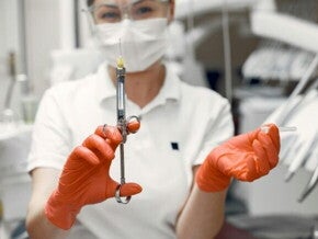 Médica usando máscara e luvas laranjas nas mãos está segurando uma injeção para aplicar a anestesia peridural em centro cirúrgico antes do parto. 