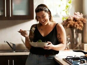 Mulher sorrindo e comendo salada na cozinha