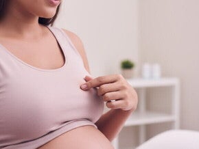 Mulher grávida toca o mamilo, explorando o engrossamento comum na gestação.