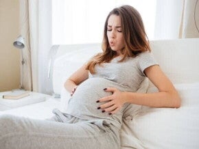 Mulher grávida deitada na cama, com as mãos na barriga e uma expressão de desconforto. A imagem ilustra o momento de sentir as contrações de treinamento, uma das sensações comuns durante a gestação. Mulher grávida deitada na cama, com as mãos na barriga e uma expressão de desconforto. A imagem ilustra o momento de sentir as contrações de treinamento, uma das sensações comuns durante a gestação.