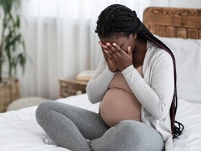 Mulher grávida sentada na cama cobrindo o rosto com as mãos. Mulher grávida sentada na cama cobrindo o rosto com as mãos.