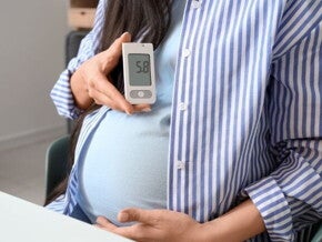Imagem de uma gestante segurando um glicosímetro com uma mão enquanto a outra mão está sustentando a parte inferior da barriga, simbolizando a atenção em relação à diabetes gestacional.