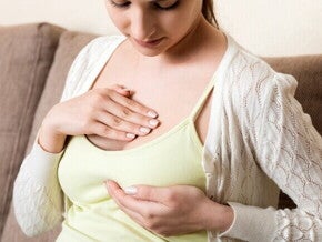 Mulher com as mãos sobre a área do peito, indicando sensibilidade e dor nos seios na gravidez, um sintoma comum do aumento da glândula mamária.
