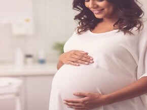 Mulher grávida mixed-race no terceiro trimestre tocando a barriga gentilmente, representando exames finais e parto.