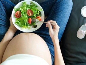 Gestante sentada em um sofá saboreando uma salada saudável