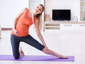 Gestante sorridente alongando em tapete de yoga dentro de casa.