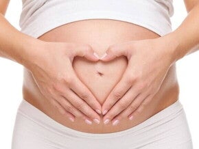 Close de mulher grávida com as mãos formando um coração sobre a barriga.