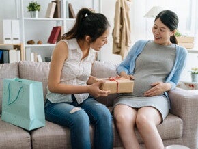 mulher grávida sentada no sofá recebe presentes de amiga em chá de fraldas mulher grávida sentada no sofá recebe presentes de amiga em chá de fraldas