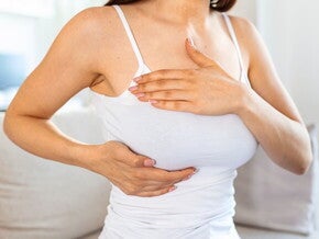 Mulher sentada no sofá apalpando as mamas