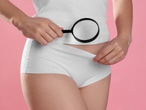 Detalhe de uma mulher segurando uma lupa sobre a região pélvica/genital
