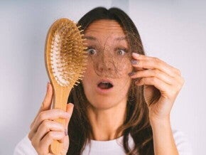 Uma mulher com expressão de surpresa segura um tufo de cabelo que se desprendeu na escova. A imagem representa o choque e a preocupação com a queda de cabelo pós-parto.