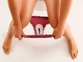 Mancha de sangramento na calcinha de uma mulher sentada no vaso sanitário.