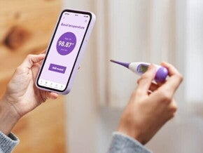 mulher segurando celular e termômetro ao monitorar temperatura basal.