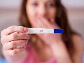 Mulher segurando teste de gravidez positivo com expressão emocionada