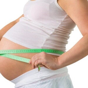 Mulher grávida de 33 semanas de gravidez medindo a circunferência da barriga com fita métrica, um marco no terceiro trimestre.