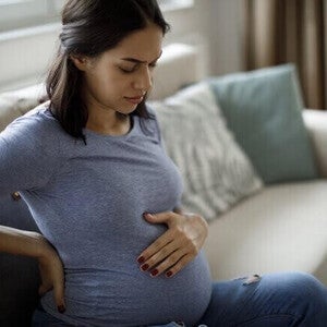 Mulher grávida com náusea, sentada no sofá