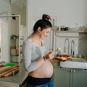 Mulher grávida sorrindo na cozinha enquanto come um doce