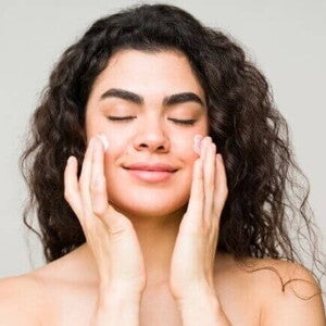 Mulher espalhando creme hidratante no rosto, de olhos fechados Mulher espalhando creme hidratante no rosto, de olhos fechados