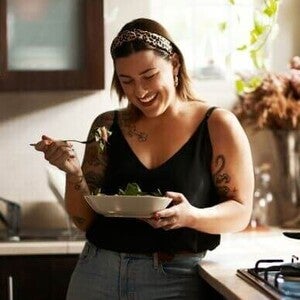Mulher sorrindo e comendo salada na cozinha
