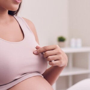 Mulher grávida toca o mamilo, explorando o engrossamento comum na gestação.