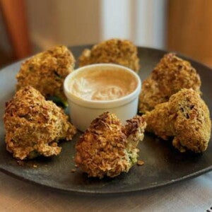 Seis Brócolis Empanado dispostos sobre um prato com um recipiente de molho ao centro