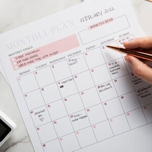 Na imagem, uma mão segura uma caneta diante de um calendário do mês Na imagem, uma mão segura uma caneta diante de um calendário do mês
