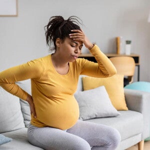 mulher grávida com uma das mãos nas costas e outra posicionada na testa, com olhos fechados e assoprando com a boca mulher grávida com uma das mãos nas costas e outra posicionada na testa, com olhos fechados e assoprando com a boca