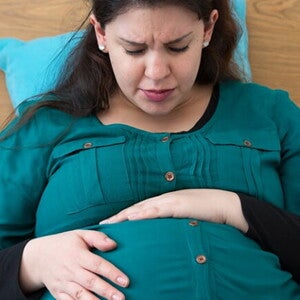 Mulher grávida sentada na cama com semblante de preocupação embalando sua barriga Mulher grávida sentada na cama com semblante de preocupação embalando sua barriga