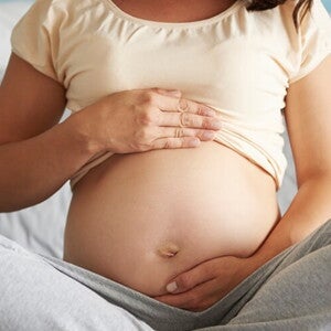 Gestante sentada na cama com as pernas cruzadas enquanto acaricia a barriga com as duas mãos. Gestante sentada na cama com as pernas cruzadas enquanto acaricia a barriga com as duas mãos.