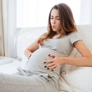 Mulher grávida deitada na cama, com as mãos na barriga e uma expressão de desconforto. A imagem ilustra o momento de sentir as contrações de treinamento, uma das sensações comuns durante a gestação.