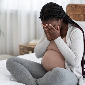 Mulher grávida sentada na cama cobrindo o rosto com as mãos. Mulher grávida sentada na cama cobrindo o rosto com as mãos.