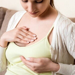 Mulher com as mãos sobre a área do peito, indicando sensibilidade e dor nos seios na gravidez, um sintoma comum do aumento da glândula mamária.