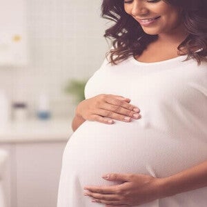 Mulher grávida mixed-race no terceiro trimestre tocando a barriga gentilmente, representando exames finais e parto.