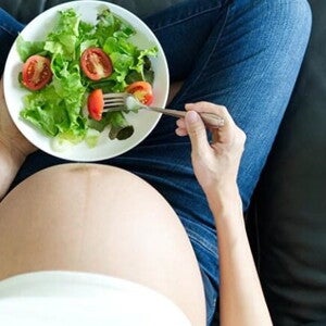 Gestante sentada em um sofá saboreando uma salada saudável Gestante sentada em um sofá saboreando uma salada saudável