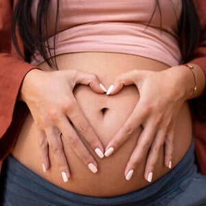 Gestante com as mãos sobre a barriga fazendo o formato de um coração com as mãos