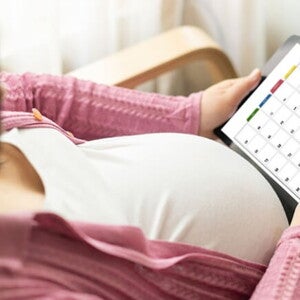 Gestante sentando em uma cadeira olhando para um calendário virtual