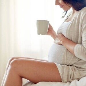 Mulher grávida sentada com uma caneca na mão Mulher grávida sentada com uma caneca na mão