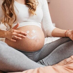 gestante aplicando creme na barriga com desenho de carinha sorridente. gestante aplicando creme na barriga com desenho de carinha sorridente.