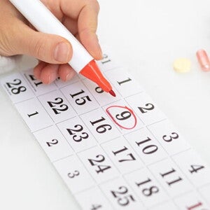 Imagem de uma pessoa fazendo anotações em um calendário em meio a comprimidos e objetos diversos Imagem de uma pessoa fazendo anotações em um calendário em meio a comprimidos e objetos diversos