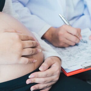 Médico com uma prancheta nas mãos fazendo anotações enquanto uma mulher grávida está sentada na cama Médico com uma prancheta nas mãos fazendo anotações enquanto uma mulher grávida está sentada na cama