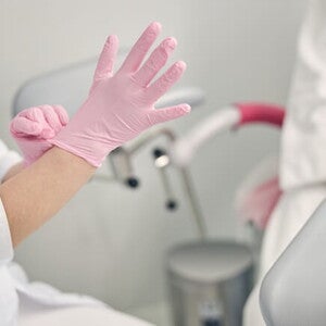 Paciente sentada em cadeira ginecologia enquanto médica se prepara para examiná-la Paciente sentada em cadeira ginecologia enquanto médica se prepara para examiná-la