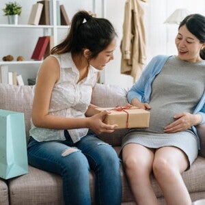 mulher grávida sentada no sofá recebe presentes de amiga em chá de fraldas mulher grávida sentada no sofá recebe presentes de amiga em chá de fraldas