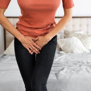 mulher com as pernas cruzadas com as mãos em cima da vagina